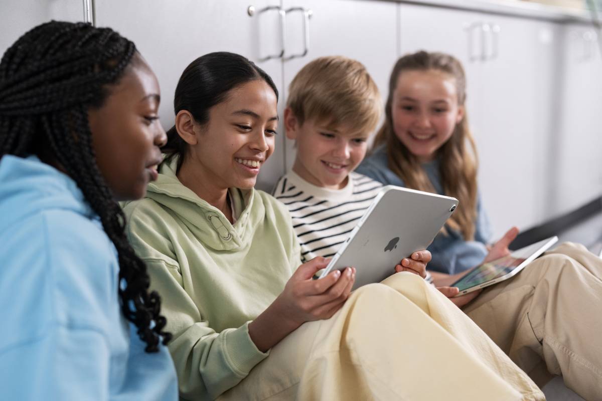 Drei Schülerinnen und ein Schüler sitzen vor einem Spint in der Schule und lernen mit dem iPad von Apple