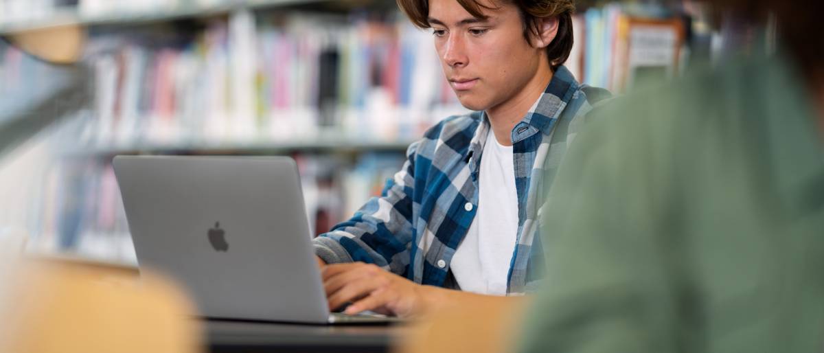 Ein Student sitzt in einer Bibliothek vor einem MacBook Air