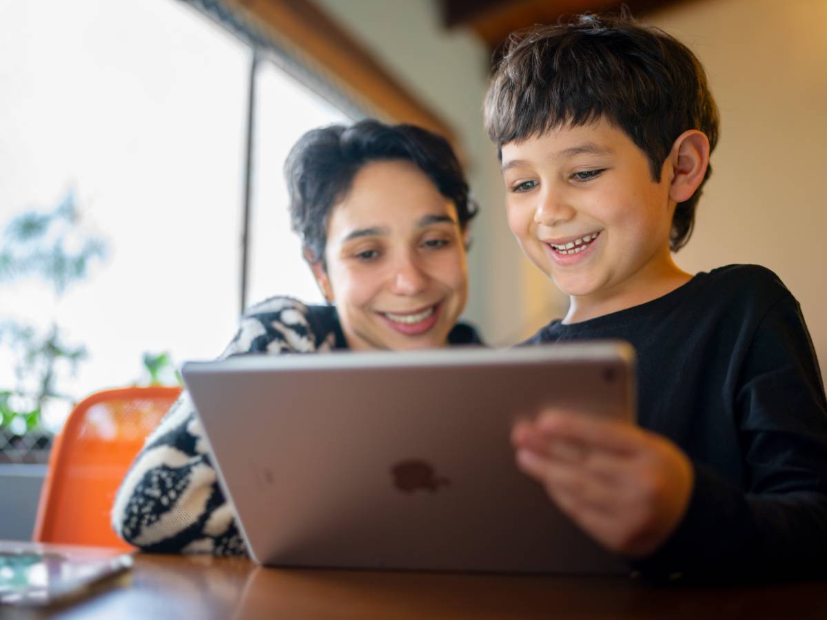 Eine Mutter und ihr Sohn im Volksschulalter bedienen in einer Wohnumgebung gemeinsam ein iPad