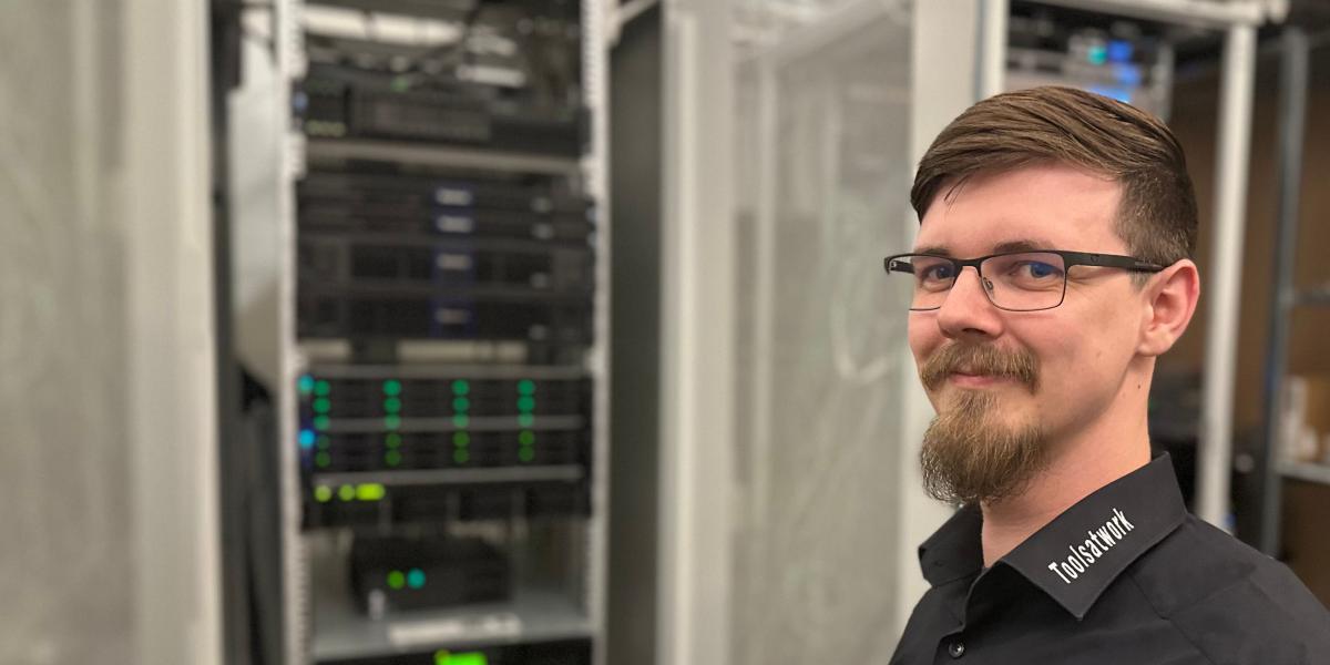 Ein Mann befindet sich vor einem Serverschrank mit zahlreichen Datenkabeln