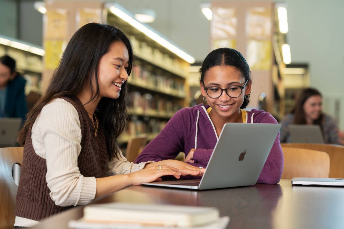 Zwei Schülerinnen arbeiten in einer Bibliothek auf einem MacBook Air