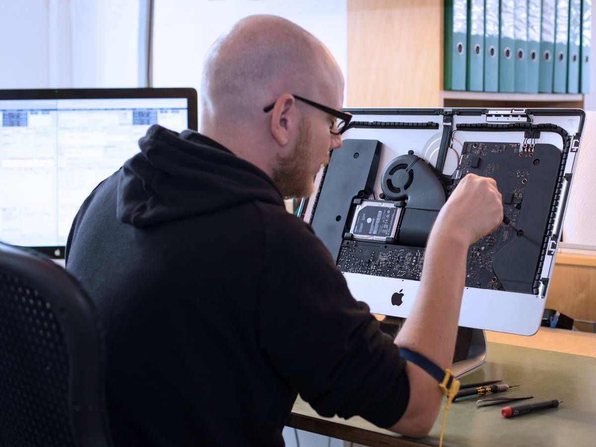 Nico Sieder, Tools at Work Spezialist im Apple Service, repariert ein MacBook, das mit geöffnetem Gehäuse auf seinem Arbeitstisch liegt